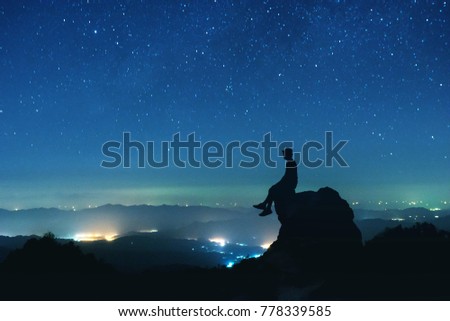 Man's silhouette sits on big rock at mountain top on background of night sky