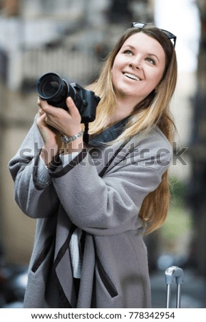 Young cheerful woman with a camera looking curious and taking pictures outdoors 