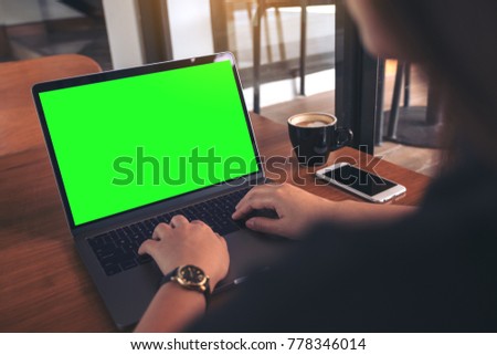 Mockup image of business woman using and typing on laptop with blank green screen , coffee cup and mobile phone on wooden table in cafe