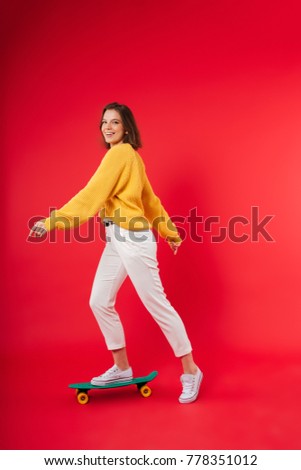 Full length portrait of a happy girl riding on a skateboard isolated over pink background