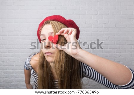 Funny young girl holding a red paper heart and laughing at the camera. Valentine's Day.