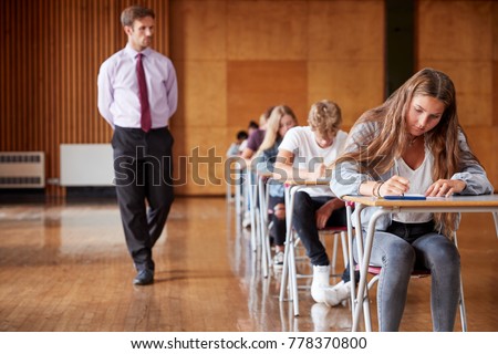Teenage Students Sitting Examination With Teacher Invigilating Royalty-Free Stock Photo #778370800