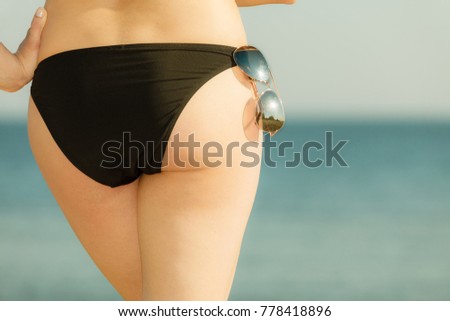 Summertime underwear, being confident during summer concept. Woman bottom bum in black bikini panties and glasses. Sea background.