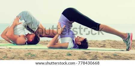 Young couple doing yoga poses sitting on sunny beach by ocean in morning