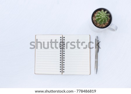 Blank open notebook with new shiny silver pen with cactus plant in white cup on white texture table background