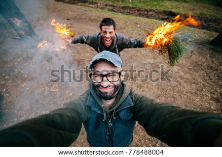 Frineds make selfie. Crazy funny boys mess around. Men at nature playing and fooling with fire. Eccentric bizarre strange unusual young guys with dirty faces mad party in forest. Burn, flame, smoke.
