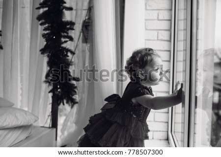 Black and white picture of a little girl standing before a window