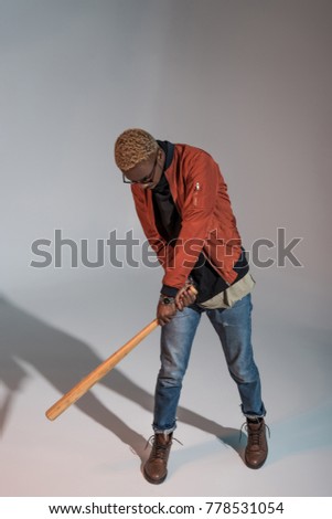 high angle view of stylish young african american man playing with baseball bat on grey