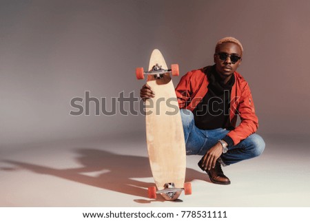 Stylish young african american skateboarder sitting and holding longboard