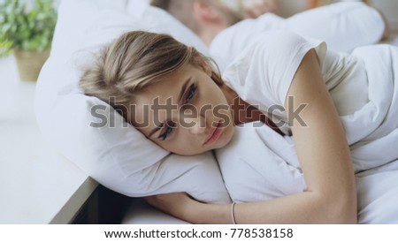 Depressed young woman lying in bed and feeeling upset after quarrel with her boylfriend in bed at home