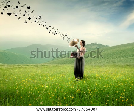 Elegant woman holding an old gramophone playing music on a green meadow