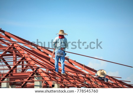 Construction welder workers installing steel frame structure of the house roof at building construction site with clouds and sky
