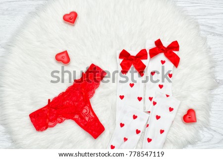 Fashion concept. Red thong panties and white stockings with bows, candles in the shape of a heart on a white fur.