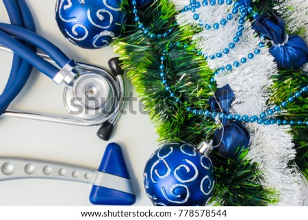 Christmas and New Year decorations near medical equipment. Neurology hummer and medical stethoscope lying near artificial snow with glitter, toys and blue balls on Christmas tree. New Year in Medicine