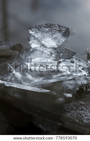 Tower of ice pieces made by a child. Transparent ice of different shapes with rough surface with daylight shining through it. Faded colors, blurred dark and light background ready for your text.