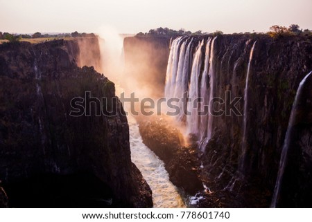 scenic picture of the victoria falls  photographed by sunset with red colors and some rocks and grass in the front of the picture (4)