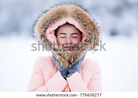 Smiling happy pretty woman in warm winter jacket outdoors enjoys winter journey, weared gloves and hood, a lot of snow, blowing snow to the camera, sparkling bengal lights Royalty-Free Stock Photo #778608277