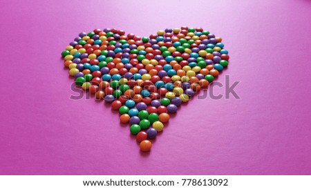 Colorful confetti candy heart shape on pink background