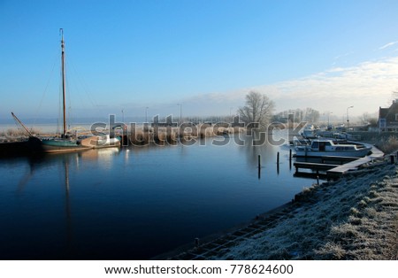 Dutch canal in the winter, frozen water and some boats in the harbour