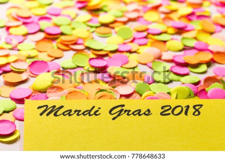 Carnival party background concept, space for text. Written the words: Mardi Gras 2018. Colorful confetti over table. Warm colors: pink, yellow and orange. Horizontal orientation, selective focus.