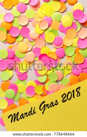 Carnival party background concept, space for text. Written the words: Mardi Gras 2018. Colorful confetti over table. Warm colors: pink, yellow and orange. Overhead, flat lay, vertical orientation.