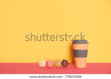 Cup of coffee to go with macaron on yellow and pink background with place for your text.