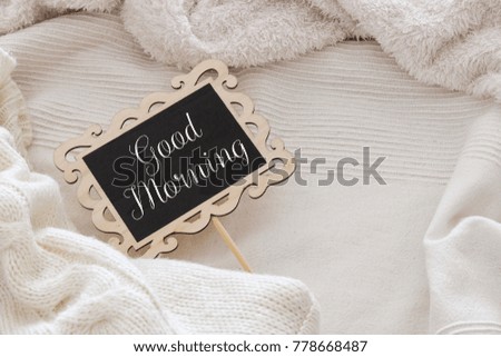 Image of chalkboard with text: GOOD MORNING over cozy and white blanket. Top view