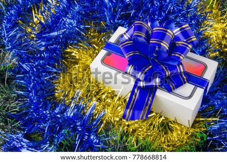 A box with a smartphone inside. Festively packed box with a popular smartphone inside on Christmas decorations.