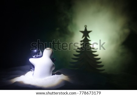 Love New Year concept. Girl and boy ceramic figures hugs each other, standing on the white snow and colored heart and Christmas tree on blurred dark background. Empty space. Hugging sculptures.