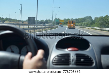 Man driving a car on a highway with other vehicles and direction signs in front of him. Blurred car interior.