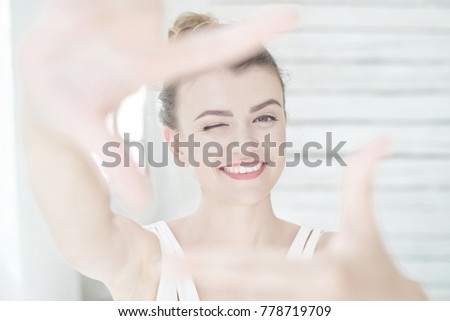 Pretty young woman making a frame gesture with her hands framing her face as she winks at the camera with a happy smile with focus to her face.