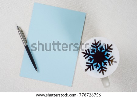 Pure blue sheet of paper on white table. Pen, coffee cup and abstract snowflake - symbol of winter, Christmas