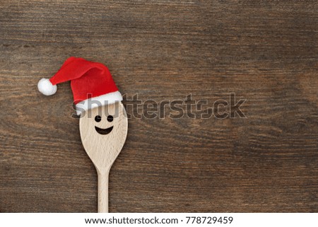Christmas background with wooden spoon in red Santa Claus hat on rustic wooden background, top view, flat lay, minimal design