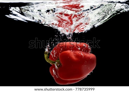 Red pepper falls into the water with a spray.
