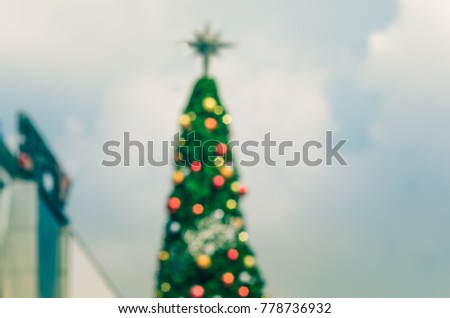 Blurred picture of Christmas tree and various colored balls. The top of it is star. It was set in the open. There is a sky and clouds background image.