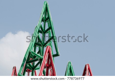 Christmas tree it is red and green made of steel. It was set in the open. There is a sky and clouds background image.