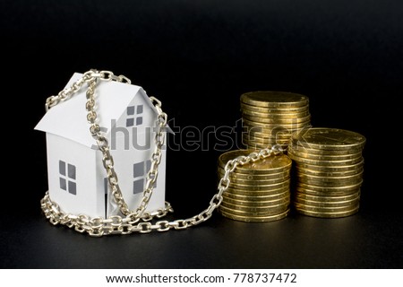 white small paper house tied with chain to the money golden coins, loan money secured by immovable property concept, close up, selective focus , blurred dark background Royalty-Free Stock Photo #778737472