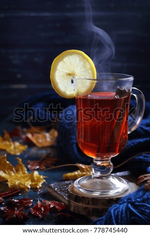 cup of hot black tea with cinnamon and lemon in autumn decorations, natural smoke