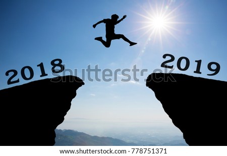 A young man jump between 2018 and 2019 years over the sun and through on the gap of hill silhouette evening colorful sky. happy new year 2019. Royalty-Free Stock Photo #778751371