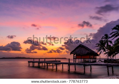 Colorful tropical sunset on one of the San Blas islands in the Caribbean Sea. Shore scene with a beach house and a jetty. Royalty-Free Stock Photo #778763773