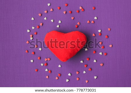 Red fabric hearts on a purple background is surrounded by candy's. Valentine's Day.