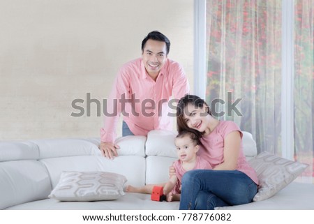 Picture of Asian parents smiling at the camera while playing with their daughter at home