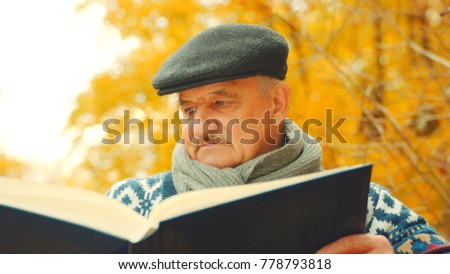 Close up of Old man watching big photo album in the autumn park