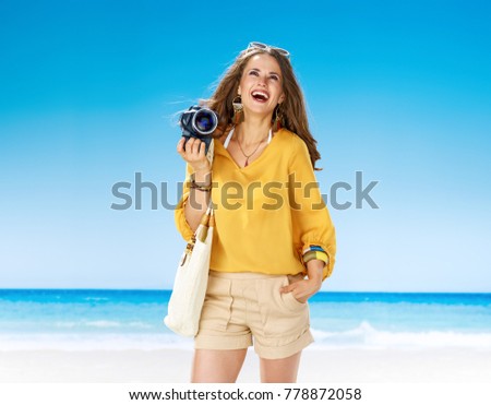 Perfect summer. smiling young woman in shorts and yellow blouse with white beach bag on the beach with digital SLR camera looking at copy space