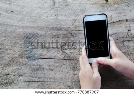 Women use smartphone with blank screen on wooden table. Copy space.