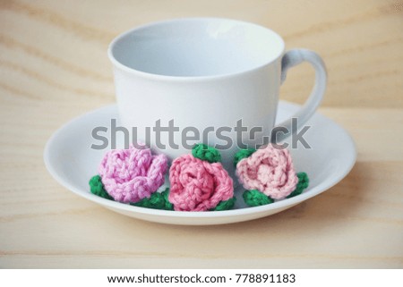 Colorful crochet flowers and white cup on wooden background, Vintage style