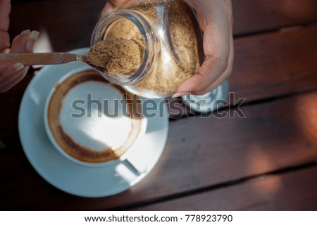 Close Up of a cropped woman pouring sugar into coffee cup. Sweetening coffee.