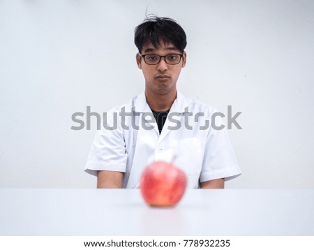 Picture of young scientist looking a blur red apple on white table