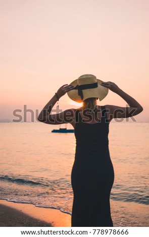Girl in a hat looks at the sunset and boat in the ocean