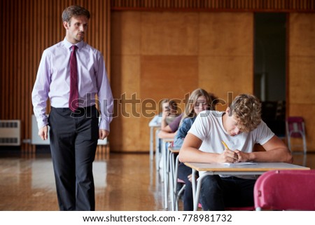 Teenage Students Sitting Examination With Teacher Invigilating Royalty-Free Stock Photo #778981732